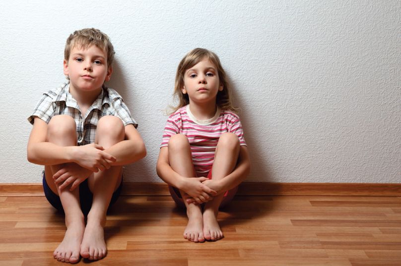 Ein Mädchen und ein Junge sitzen mit angewinkelten Knien auf dem Fußboden