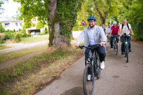 OB auf dem Fahrrad, einige Radler hinter ihm radeln mit.