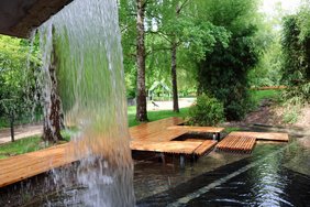 Im Vordergrund der Wasserstrahl eines Wasserfalls, im Hintergrund ein Wasserbecken mit mehreren Flößen aus Holz