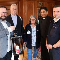 Oberbürgermeister Jan Rothenbacher nimmt von Roberto Kalz das Friedenslicht in einer Laterne entgegen. Dahinter die drei weiteren Personen. 