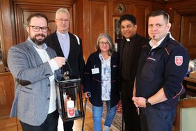 Oberbürgermeister Jan Rothenbacher nimmt von Roberto Kalz das Friedenslicht in einer Laterne entgegen. Dahinter die drei weiteren Personen. 