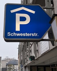 Im Bild ist das Leuchtschild vor dem Parkhauseingang abgebildet: ein großes P mit Dach auf blauem Grund, darunter der Schriftzug "Schwesterstraße". 