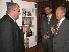 Dr. Fassl, Vorsitzender Engelhard und OB Dr. Holzinger vor einer Schautafel der Ausstellung in der Rathaushalle