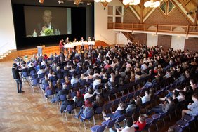 Blick hinunter auf Podium und viele Reihen mit Zuhörerinnen und Zuhörern von der Empore aus