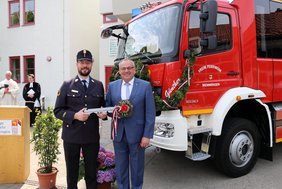 OB und Stadtbrandrat mit großem, blumengeschmücktem Holzschlüssel vor dem Löschfahrzeug