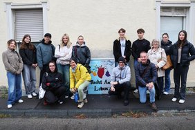 Die Gruppe rund um einen Stromkasten mit der Aufschrift "Recht auf Leben" und einem Herz, aus dem auf einer blauen Seite eine blühende Blume ragt, auf einer grauen Seite eine verwelkte Blume. 