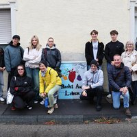 Die Gruppe rund um einen Stromkasten mit der Aufschrift "Recht auf Leben" und einem Herz, aus dem auf einer blauen Seite eine blühende Blume ragt, auf einer grauen Seite eine verwelkte Blume. 
