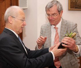 Als Geschenk überreicht Dr. Rehm Dr. Holzinger ein Flasche Wein.