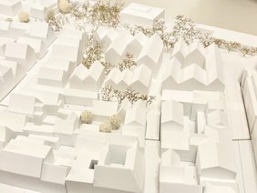 Hinter den drei Personen stehen Schautafeln mit Plänen. Dazu ein Schild: "1. Platz"