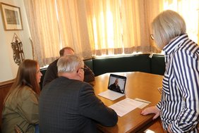 Auf einem Tisch steht ein IPad mit dem Gesicht von Atroshenko. Rundherum sitzen und stehen OB schilder und die anderen Anwesenden.