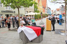 Zu sehen ist ein Überblick über die Feierstunde: das noch abgedeckte Modell im Vordergrund, OB Holzinger am Rednerpult und die Gäste rundherum