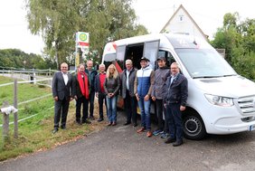 Die Gruppe steht vor einem Kleinbus. Im Hintergrund ist das Haltestellenschild "Am Stadtweiher" zu sehen.