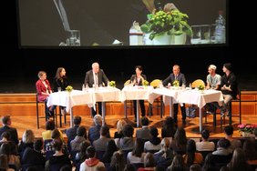 Gezeigt wird das Podium auf der Bühne der Stadthalle. Im Vordergrund die Zuhörer.