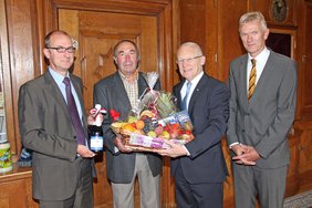 Im Amtszimmer stehen die vier Herren nebeneinander. Herr Sternath hält als Präsent eine Flasche Sekt in Händen. Werner Baader und OB Holzinger tragen gemeinsam einen großen Geschenkkorb.