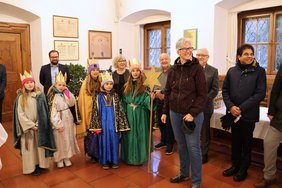Eine Gruppe von fünf Sternsingerinnen sprechen die Segenswünsche, um sie herum OB Rothenbacher und Pater Joshy Palakunnel.