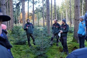 Die Männer stehen inmitten der Bäume, von hinten sind die Stadträte zu sehen.