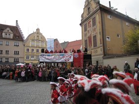 Blick über die Teen- und Kindergarde auf den 11er Rat auf seinem historischen Brauerei-Bus, dazu die Schaulustigen.
