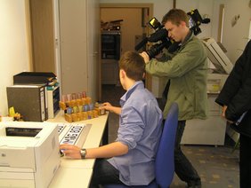 Auszubildender Julian Rapp, in der KFZ-Zulassungsstelle, wie er beim Schilder stempeln gefilmt wird.