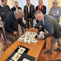 Zwei Männer sind am Tisch über ein Modell gebeugt, daneben drei weitere Modelle. Im Hintergrund stehen mehrere Personen, Mitglieder des Gestaltungsbeirats.