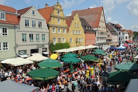 Von oben aus dem 2. Stock der Kramerzunft aus fotografiert. Viele Menschen und Sonnenschirme auf dem Platz vor den bunten Fassaden der Weinmarkt-Häuser. 
