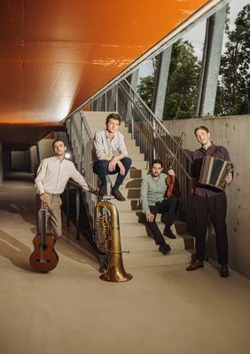 Vier Männer mit Instrumenten, stehend oder auf einer Treppe sitzend