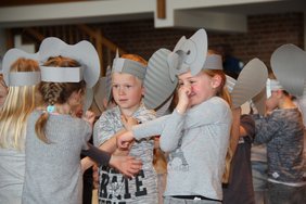 Die Elefantenkinder tragen große graue Ohren aus Wellpappe. Sie fassen mit einer Hand ihre Nase und stecken die andere Hand durch den dadurch enstandenen Armkreis, um einen Rüssel zu spielen.