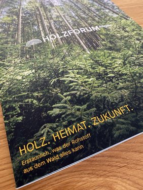 Das Cover zeigt hohe Bäume in einem Wald, unten wachsen junge Bäume nach. Text: Blickwinkel, Geschichten, Ideen. Holzforum Allgäu. Holz-Heimat-Zukunft-Erstaunlich, was der Rohstoff aus dem Wald alles kann. www.holzforum-allgaeu.de