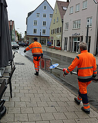 Zwei Bauhof-Mitarbeiter tragen ein Schild weg. 