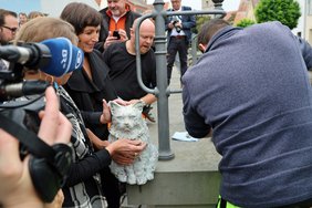 Die Künstlerin hält die Skulptur in Händen, um sie herum viele Menschen und Kameras. 