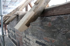 Gezeigt wird ein alter Balken, der an einem kleinen Stück durch neues Holz ausgebessert worden ist.