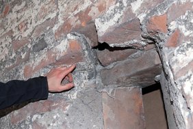 Ein Finger deutet auf den Sturz einer Schießscharte, wo die abgeschrägten Zeigel zu erkennen sind.