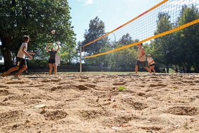 Sandplatz mit Netz, vier Sportlerinnen und Sportler spielen gerade.