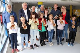 Die Kinder stehen in der ersten Reihe mit an den Mund angelegten Trompeten, die weiteren Personen in der Reihe dahinter. 