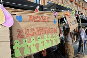 Plakat mit Aufschrift: Besser zusammen und viele Figuren, die sich die Hand reichen