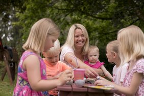 Frauen und Kinder sitzen im Freien an einer Bank.