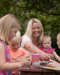 Frauen und Kinder sitzen im Freien an einer Bank.