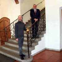 Die beiden Herren stehen am Geländer der Rathaustreppe im aktuell notwendigen Abstand von mindestens 1,5 Metern.