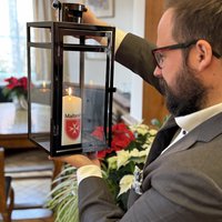 OB Jan Rothenbacher ist seitlich zu sehen, er hält die Laterne mit der Kerze mit beiden Händen etwa auf Augenhöhe und schaut die Kerze an 