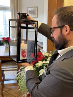 OB Jan Rothenbacher ist seitlich zu sehen, er hält die Laterne mit der Kerze mit beiden Händen etwa auf Augenhöhe und schaut die Kerze an 