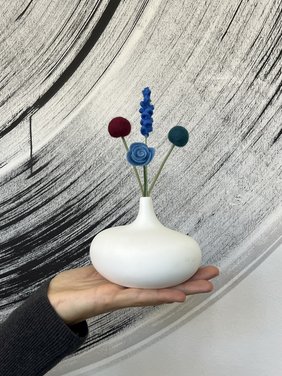 Eine Hand hält eine Vase mit gefilzten Blumen