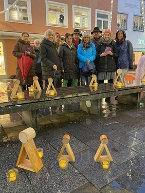 Vor der Gruppe sind Teelichter und hölzerne Gedenkfiguren.