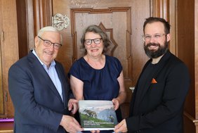 Gruppenfoto der drei Personen, alle drei halten gemeinsam ein Buchexemplar. 