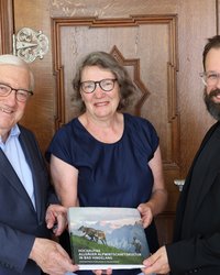 Gruppenfoto der drei Personen, alle drei halten gemeinsam ein Buchexemplar. 