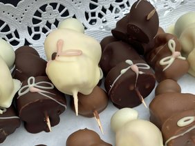 Abgebildet sind Früchte in dunkler, weißer und Vollmilchschokolade mit Verzierung. 