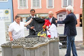 Zu sehen sind die vier Personen hinter dem bereits teilweise enthüllten Stadtmodell. Sie ziehen ein Tuch von dem Modell, das das Memminger Stadtwappen zeigt.