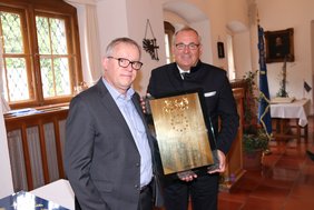 Die zwei Herren halten den Preis in Händen: Die Ehrenplakette ist eine große, rechteckige, spiegelnde Scheibe. Sie kann wie ein Bild an die Wand gehängt werden.