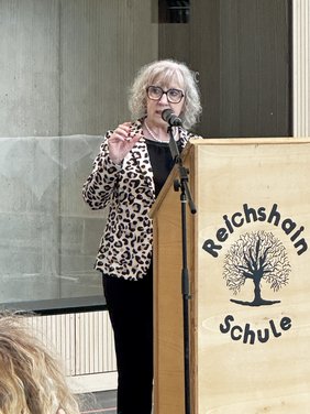 Die Bürgermeisterin am Rednerpult, das die Aufschrift "Reichshainschule" trägt.