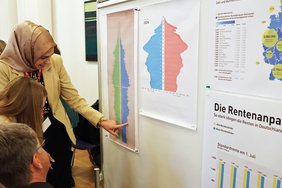 Sie zeigt zwei Besuchern etwas auf der Messetafel an ihrem Stand