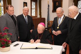 Bischof Konrad trägt sich in das Goldene Buch ein. Die Ehrengäste schauen ihm zusammen mit OB Dr. Holzinger über die Schulter