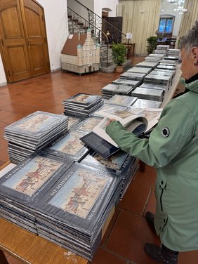 Eine lange Tischreihe mit Büchern bepackt, eine Frau von hinten, die in einem Buch blättert.